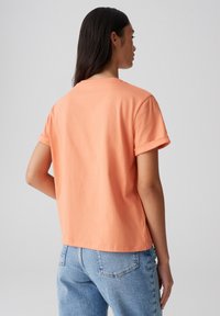 T-shirt a maniche corte in cotone corallo con maniche arrotolate e una vestibilità rilassata, abbinato a jeans in denim blu chiaro. Design semplice e minimal.