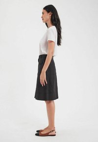 Jupe en lin noir avec une coupe droite et des poches latérales, associée à un t-shirt blanc et des ballerines marron avec un bout noir.