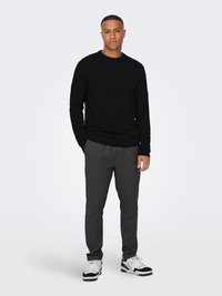 Black textured sweater with round neckline, paired with gray pinstriped pants and white sneakers with black accents.