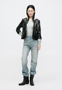 Μαύρο δερμάτινο κοντό μπουφάν πάνω από γκρι πουλόβερ, συνδυασμένο με ανοιχτό μπλε ψηλόμεσα τζιν και μαύρες μπότες μέχρι τον αστράγαλο. Απλός, casual σχεδιασμός.