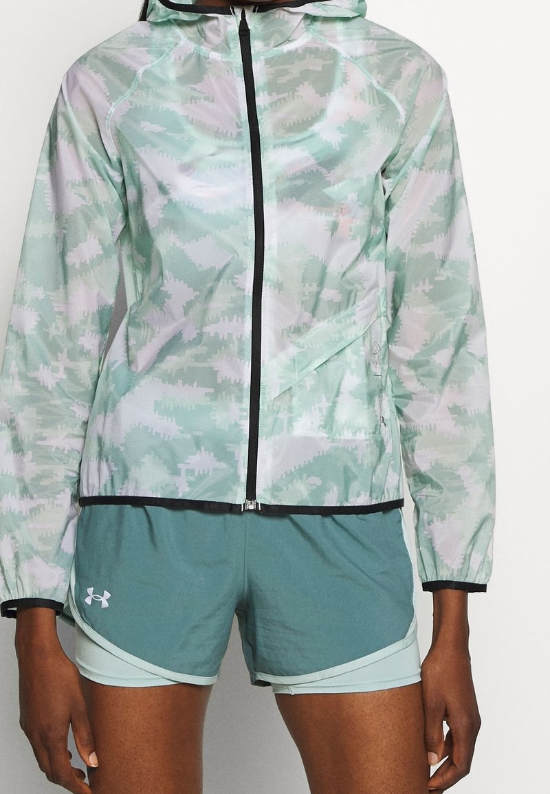Chaqueta con capucha ligera en un patrón abstracto de verde menta y blanco, que presenta un cierre frontal, ribetes en negro contrastante y tejido transpirable.