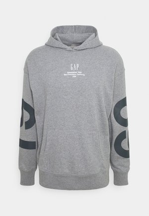Grauer Hoodie mit Fronttasche, Kapuze, GAP-Logo und Text auf der Brust sowie großen schwarzen Buchstaben auf beiden Ärmeln.