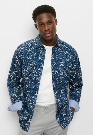 Blaues Hemd mit floralem Muster aus Baumwollstoff, mit durchgehender Knopfleiste und kontrastierenden hellblauen Manschetten. Kombiniert mit hellgrauer Hose.