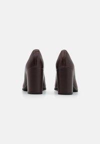 Zapatos de tacón alto de cuero burdeos con punta afilada y tacones cuadrados gruesos, que presentan una textura suave y un diseño minimalista.
