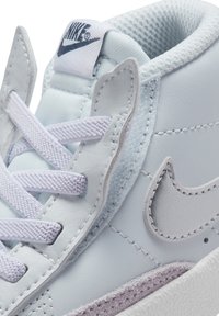 Baskets en cuir bleu clair avec des accents texturés, lacets violets et logo Nike gris. Comprend un col rembourré et une semelle intermédiaire contrastante.