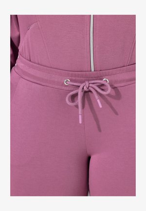 Tutina viola con una texture liscia, chiusura frontale con zip, vita regolabile con cordino e dettagli rosa, e tasche laterali.