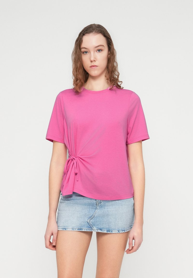 Pinkes T-Shirt mit kurzen Ärmeln und seitlichem Knotendetail aus weichem Stoff, kombiniert mit einem Jeansminirock. Glatte Textur und legere Passform.