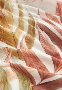 Tissu doux avec un motif de grandes feuilles allongées aux teintes de brun, beige et vert pale sur un fond blanc.