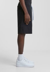 Pantalones cortos de algodón negros con una cinturilla elástica y un cordón azul claro. Estilizados con zapatillas blancas y calcetas de longitud hasta el tobillo.