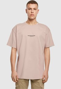 Light pink oversized t-shirt made of cotton, featuring a crew neck and short sleeves. Black text reading "METAMORPHOSIS" on the front.