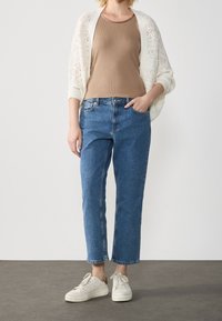 Krémový pletený svetr přes těsné béžové tílko, doplněný o džíny s rovnými nohavicemi a bílé tenisky. Elegantní, neformální outfit.