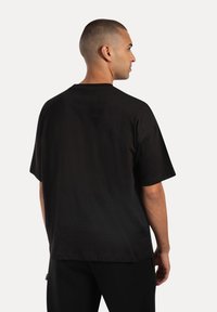 T-shirt in cotone nero con vestibilità morbida, maniche corte e scollatura a girocollo. Texture liscia con dettagli di design minimi.