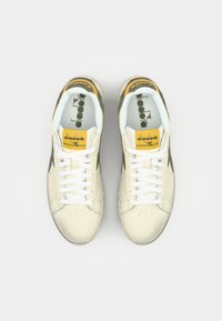 White leather sneakers with yellow and green accents. Features a perforated toe, white laces, and a padded tongue with logo.