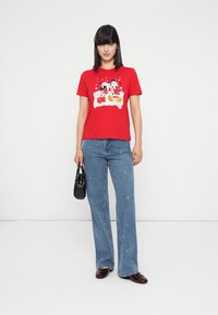 Red cotton t-shirt with a graphic print featuring characters and cakes, paired with light blue flared jeans and a small black handbag.