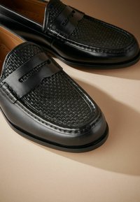 Zwarte leren loafers met een geweven textuur op de neus en een gladde afwerking. Voorzien van een subtiele accentband en een ronde, duurzame zool.