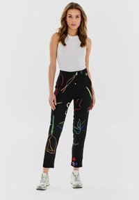 Czarne spodnie z kolorowymi kwiatowymi i abstrakcyjnymi wzorami, z wysokim stanem i dopasowanym krojem, o prostej nogawce. Noszone z białym topem bez rękawów.