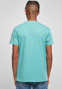 Tricou din bumbac turcoaz, cu mâneci scurte, guler rotund și o textură netedă, ce prezintă o croială relaxată și un design simplu.