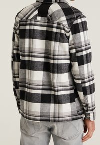 Zwart-wit geruite flanellen shirt met een kraag en knopenmanchetten, met een gestructureerde stof en een rechte zoom, weergegeven vanuit de achterkant.