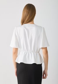 Bílý peplum top s krátkými nabíranými rukávy a detailním drapením v pase, nošený přes černou sukni. Hladká látka s jemným leskem.