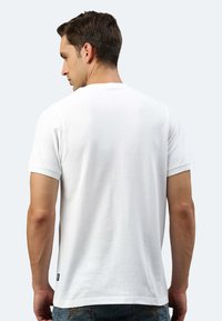 Maglietta a maniche corte bianca con collo girocollo, realizzata in cotone e caratterizzata da una vestibilità dritta. Etichetta del marchio visibile sul lato sinistro vicino all'orlo.