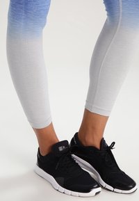 Leggings leggeri con una sfumatura da blu a bianco, abbinati a scarpe da ginnastica nere con una suola flessibile e un branding sottile.