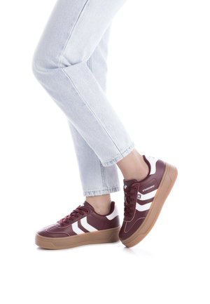 Zapatillas burdeos con rayas blancas, suela de goma y parte superior sintética texturizada. Presenta cordones y un cuello acolchado. Combinadas con jeans de lavado claro.