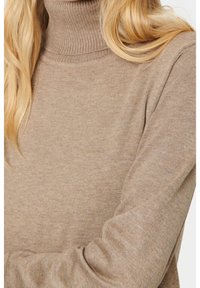 Pull à col roulé beige en tricot avec un col côtelé et des manches longues, présentant une texture fine et une silhouette ajustée.
