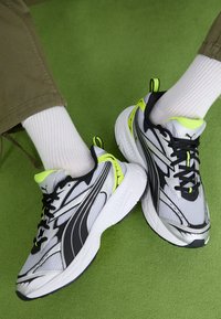 Szürke és fekete sportcipők neon zöld kiegészítőkkel. Lélegző hálós felsőrész, vastag fehér talp és fekete fűző. Bordás fehér zoknik.