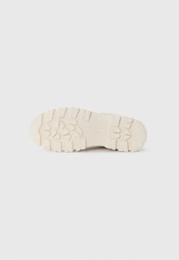 Off-white joggesåle med robust mønster, med hevede knotter for grep; laget av slitesterkt gummi materiale.