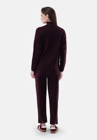 Burgunderfarbener gestrickter Pullover und passende Hose mit seitlichen Schlitzen. Weicher Stoff, lockere Passform und kombiniert mit braunen und weißen Sneakers.