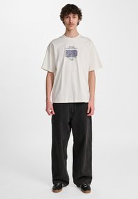 Crème kleurige t-shirt met korte mouwen en grafische print; ruime pasvorm. Draag met zwarte wijde jeans en zwarte schoenen. Minimalistische stijl en casual ontwerp.