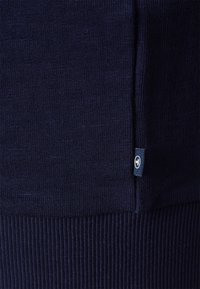 Suéter de punto azul marino con bajo acanalado, textura suave y una pequeña etiqueta con el logo cosida en la costura lateral inferior.