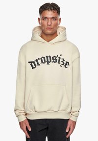 Cremefarbene Kapuzenjacke aus Fleece-Material. Mit schwarzem Text "dropsize" auf der Vorderseite, großer Tasche und Kapuze mit Zugbändern.