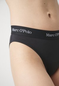Culottes hipster en coton noir avec une large ceinture noire arborant le logo blanc "Marc O'Polo". Texture lisse, conçues pour le confort.