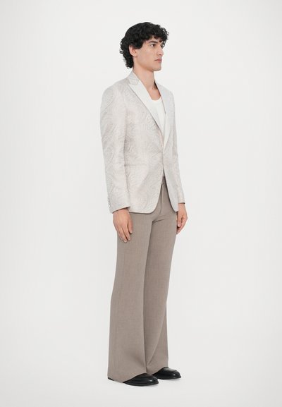 Light gray paisley-patterned blazer with a satin finish, paired with beige wide-leg pants and black shoes. Model stands in profile.
