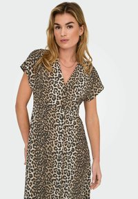 Robe à imprimé léopard avec des manches courtes et flottantes, décolleté en V et détails de boutons. Fabriquée en tissu léger dans des tons beige, marron et noir.