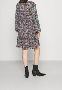 Musta kukkamekko värikkäillä kuvioilla. Ominaisuuksiin kuuluvat pitkät hihat, levenevä helma ja mustat nilkkasaappaat. Sujuva kangasrakenteeltaan.