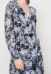 Kwiatowa sukienka o kroju kopertowym z przezroczystego materiału, z jasnoniebieskim tłem i czarnymi oraz fioletowymi kwiatami. Długie rękawy zebrane u mankietów.