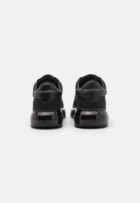 Juodos sportbačiai su lygiu paviršiumi, apvalia forma ir blizgiais guminiais padais. turi paminkštintą apykaklę ir iškeltą logotipo detalę ant kulno.