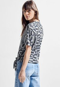 Grå og hvid mønstret t-shirt med korte ærmer og en bånddetalje i taljen, parret med lyseblå denimshorts.