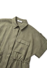 Olivově zelená lněná košile s límečkem, přední kapsou, krátkými rukávy a stažením v pase. Obsahuje boční zip pro zapínání.