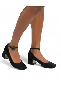 Décolleté neri in suede con punta quadrata e tacco largo. Caratterizzati da una cinturini alla caviglia con una fibbia decorativa. Texture liscia, design minimalista.