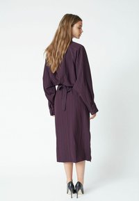 Long, dark purple dress with vertical pinstripes, long sleeves, and a tied waist. Features a straight silhouette and falls below the knee.