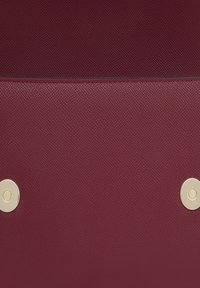 Bolso de cuero texturizado burdeos que presenta una sección superior lisa, dos broches circulares dorados y un diseño elegante.