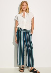 Biała lniana koszula z krótkim rękawem z detalami guzika, w połączeniu z szerokimi spodniami z pionowymi zielonymi, granatowymi i białymi paskami oraz elastycznym pasem.