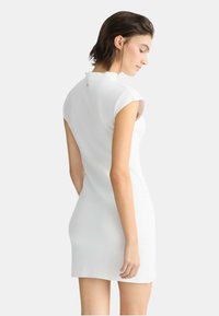Abito bianco aderente con maniche a cappuccio, dettagli con bottoni lungo la schiena e un tessuto liscio e strutturato. Design minimalista, senza motivi o ornamenti.