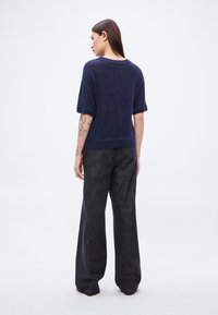 Πλεκτό πουλόβερ σε ναυτικό μπλε με κοντά μανίκια, υφή και ριμπ στα τελειώματα, συνδυασμένο με παντελόνι φαρδύ σε σκουρόγκρι απόχρωση με διακριτικό μοτίβο.