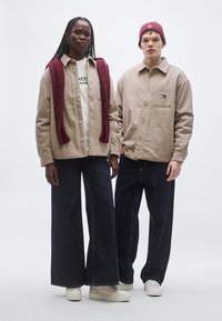 Két modell visel hétköznapi ruházatot: világosbarna kockás inget, krémszínű inget, sötét, széles szárú farmert, valamint bordó kötött sálat és sapkát.