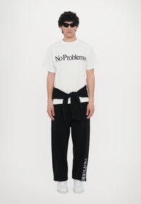 White cotton t-shirt with black "No Problemo" text, black sweatpants with white "notologie" print, and white sneakers. Styled with a black sweater tied around waist.