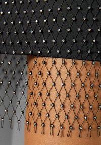 Svart nätliknande tyg med glittrande rhinestones arrangerade i ett diamantmönster, med en mjuk textur och en delikat fransdetalj.